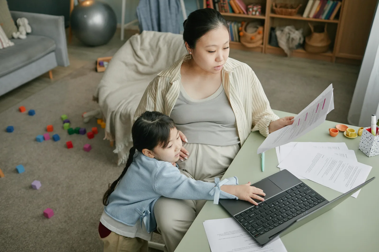 Parent working on a laptop at home while a young child plays nearby